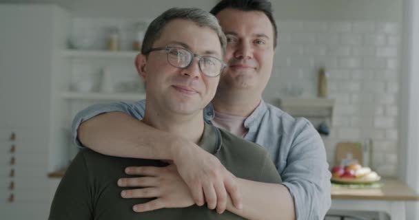 キッチンに立っている幸せなゲイカップルのゆっくりとした動きの肖像画は カメラを見ている笑顔を抱きしめます 同様の性関係と家族生活の概念 — ストック動画