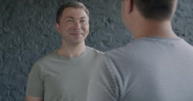 Eşcinsel bir adamı kucaklayan, gülümseyen ve evde kameraya bakan bir adamın yavaş çekim portresi. LGBTQ romantizmi ve mutlu çift konsepti.