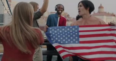 Ağır çekim heyecanlı gençlik çatıdaki partide Amerikan bayrağıyla dans ederek kutlamanın tadını çıkarıyor. Erkekler ve kadınlar şık kıyafetler giyip birlikte eğleniyorlar..