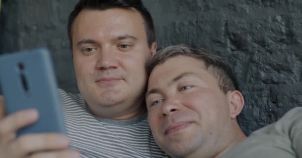 这对快乐的同性恋夫妇在卧室里用智能手机应用程序聊天 微笑着躺在床上进行特写 现代小玩意和Lgbtq概念 — 图库视频影像