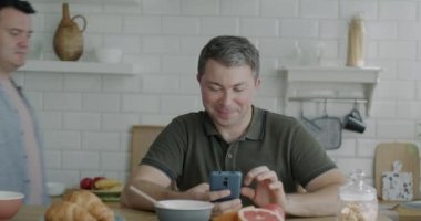 Homoseksüel bir adam, erkek arkadaşı eve gelip çevrimiçi içeriği izlerken akıllı telefon kullanıyor. Gadget ve aynı cinsiyet ilişkisi kavramı.
