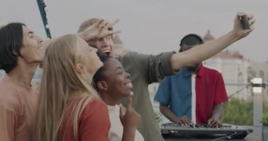 Akıllı telefon kamerasına poz veren mutlu arkadaşlar selfie çekiyorlar çatıdaki partide dans ederken eğleniyorlar. Modern teknoloji ve fotoğraf konsepti.