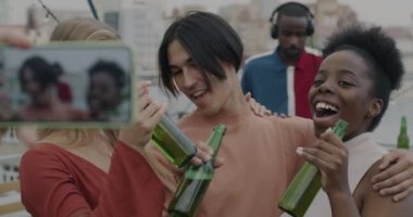 Bira şişeleri olan bir grup arkadaş akıllı telefon kamerasına poz vererek çatı partisinin tadını çıkarıyorlar. Arka planda çalışan profesyonel DJ.