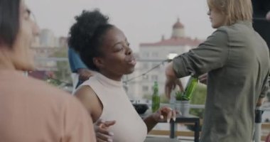 Yaz günü çatıdaki partiden keyif alan ve elinde şişelerle dans eden çok kültürlü gençlerden oluşan yavaş bir grup. Kutlama ve eğlence konsepti.