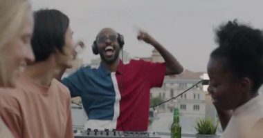 Heyecanlı Afrikalı Amerikalı DJ çatıdaki partide arkadaşlarıyla dans ederek festival etkinliğini kutluyor. Çeşitli insanlar birlikte eğleniyor..