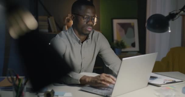 アフリカ系アメリカ人の従業員はラップトップで働いており ダークオフィスのナイトシフトの仕事に集中していた 成功した人とプロの職業コンセプト — ストック動画