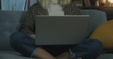 Geceleri evdeki kanepede dizüstü bilgisayarla çalışan genç ve güzel bir kadının portresi. Serbest meslek ve modern teknoloji konsepti.