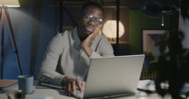 Afrika kökenli Amerikalı iş adamı masada uyuyor sonra uyanıyor ve geceleri ofiste dizüstü bilgisayarla çalışıyor. Aşırı çalışma ve insanların konsepti.