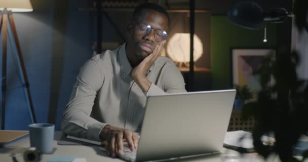 アフリカ系アメリカ人の実業家が机に座って寝てから目を覚まし 夜はオフィスでラップトップと仕事をする 過労と人々のコンセプト — ストック動画