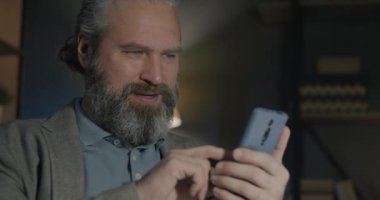 Başarılı bir iş adamı akıllı telefon kullanıyor ve gülümsüyor karanlık ofiste tatmin oluyor. Profesyonel iletişim ve olumlu duygu kavramı.