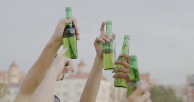 İnsanlar çatıda dans ederken elleri bira şişeleriyle gökyüzünde hareket ediyor. İçecek ve alkollü içecek konsepti.