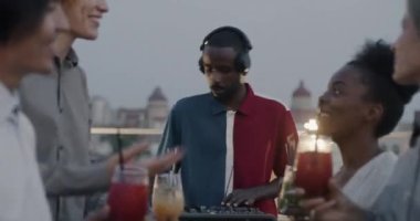 Mutlu erkek ve kadın öğrenciler kadehlerini DJ ile tokuşturarak çatı katındaki partide içki içip dans ediyorlar. Duygu ve festival konsepti.