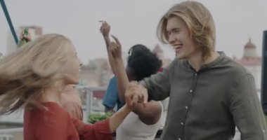 Çatıda dans eden kaygısız çiftin yavaş çekimleri. Arkadaşları gülerek birlikte eğleniyorlar. Modern yaşam tarzı ve milenyum konsepti.