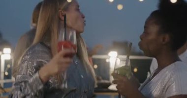 Genç Afro-Amerikan ve Kafkas dansçı kadınlar açık hava partisinde kokteyllerle kutlama yapıyorlar. Bayanlar kadehleri tokuştururken.