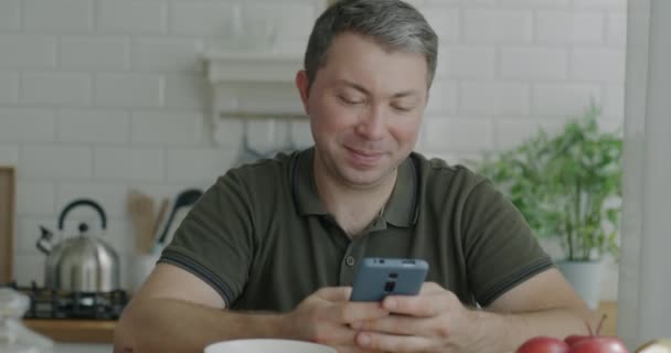 Веселый Человек Использующий Смс Смартфона Наслаждающийся Социальными Сетями Сидя Кухонным — стоковое видео