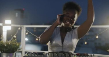 Afrika kökenli Amerikalı kadın DJ 'den uzaklaşırken insanlar çatıda dans ederken müziği karıştırıyor. Modern yaşam tarzı ve eğlenceli aktivite konsepti.