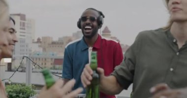 Genç erkekler ve kadınlar çatıda alkolle dans ederken enerjik DJ müziği karıştırıyor. Moda kıyafetleri içinde neşeli insanlar dışarıda parti yapıyor..