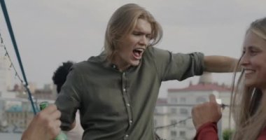 Neşeli öğrenciler, kadın ve erkek, ellerinde şişelerle dans ederek çatıda eğleniyorlar. Tatil ve eğlence konsepti.