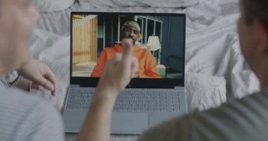 Eşcinsel çift dizüstü bilgisayarlarıyla ekranda yatakta oturan Afro-Amerikan bir adamla konuşurken video görüşmesi yapıyor. Sanal iletişim ve LGBT topluluk kavramı.