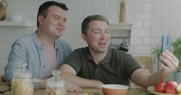肯定是同性伴侣在网上聊天 挥手打来视频电话 坐在厨房桌子旁 男人们在早餐时拥抱在一起聊天 — 图库视频影像