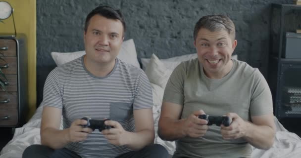 幸せなゲイカップルの肖像画は ジョイスティックを使用してオンラインビデオゲームをプレイし ベッドルームで楽しんでカメラを見ています ゲーム技術とLgbtqコンセプト — ストック動画
