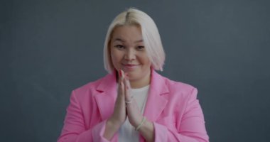 Akıllı Asyalı kadının yavaş çekimde çekilmiş portresi. El masajı yapıyor, kaşlarını kaldırıyor ve gri arka plandaki kameraya bakıyor. İnsanlar ve duygu kavramı.