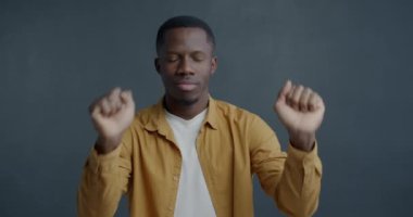 Kapalı gözlerle dans eden mutlu Afro-Amerikalı adamın yavaş çekim portresi. Gri arka planda müzik dinlemekten keyif alıyor. Halk ve gençlik kültürü kavramı.