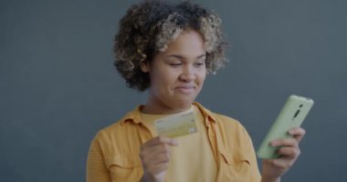 Akıllı telefon ve kredi kartıyla internetten alışveriş yapan mutlu Afrikalı Amerikalı kadının yavaş çekimde portresi. İnsanlar ve modern teknoloji kavramı.
