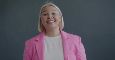 Yavaş çekimde kameraya dikkatle bakan neşeli Asyalı kadının portresi gri arka planda dürbün hareketi yapıyor. İnsanlar ve vücut dili kavramı.