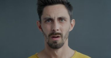 Gri arka planda kafa karışıklığını ifade eden utangaç bir gencin yüzüne dokunuşunun yavaş çekim portresi. Duygular ve yüz hareketi kavramı.