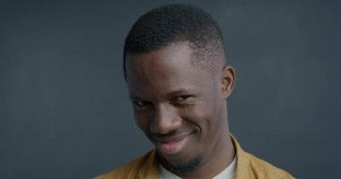 Utangaç Afrikalı Amerikalı bir adamın kameraya bakarken çekilmiş yavaş çekim portresi gri arka planda mütevazı bakışlar atıyor. İnsanlar ve yüz ifadesi kavramı.