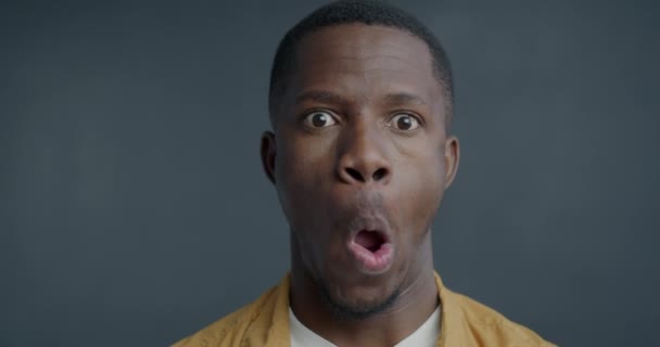 在特写的慢镜头下 一个嬉闹的非裔美国人在灰色背景下看着相机 做出滑稽的脸 人与面部表情概念 — 图库视频影像