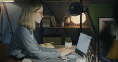 Dizüstü bilgisayarla çalışan serbest çalışan genç bir kadının ek görüntüsü akşamları evde işe odaklanmış durumda. Serbest meslek ve bilgisayar işi kavramı.