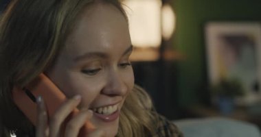 Cep telefonuyla konuşan neşeli genç bayanın yakın plan portresi. Geceleri evde sohbetin keyfini çıkarıyor. İnsanlar ve cep telefonu iletişim kavramı.