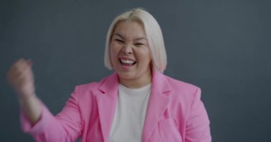 Aşırı mutlu Asyalı kadının gri arka planda başarıyı kutlayan ağır çekimde portresi. Pozitif duygu ve insanların kavramı.