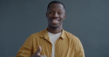 Afro-Amerikan mutlu bir adamın el hareketi ve gri arka planda gülümseme gösteren yavaş çekim portresi. İnsanlar ve olumlu duygu kavramı.