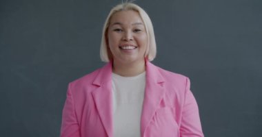 Güzel hediye kutusunu tutan neşeli Asyalı kadının yavaş çekimde çekilmiş portresi gri arka planda kameraya baktığını gösteriyor. Hediye ve tatil konsepti.