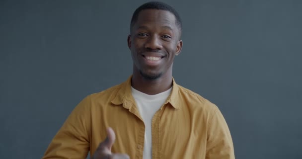 ハッピーなアフリカ系アメリカ人男性のスローモーション肖像画は 親指の手のジェスチャーを示し 灰色の背景に微笑んでいます 人とポジティブな感情のコンセプト — ストック動画
