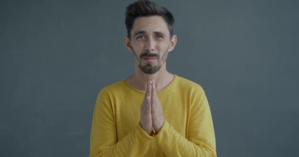 祈りのジェスチャーを作り 灰色の背景に沈黙を求める唇に触れる若者のゆっくりとした動きの肖像画 身体言語と人間の感情コンセプト — ストック動画