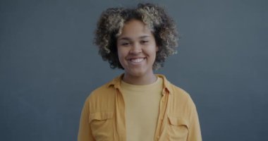 Afro-Amerikalı neşeli blog yazarının yavaş çekim portresi gri arka planda gülümseyen tabelayı işaret ediyor. Bloglama ve sosyal medya kavramı.