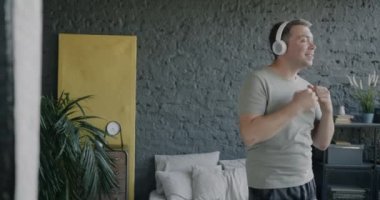 Yatak odasında kulaklık takarak dans eden kaygısız genç adamın yavaş çekimde portresi. Yaşam tarzı ve eğlence konsepti.