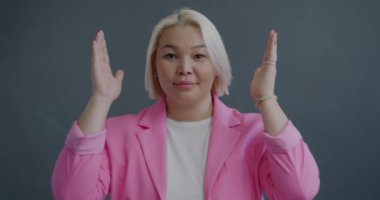 Gri arka planda kameraya bakarak saklambaç oynayan neşeli Asyalı kadının yavaş çekim portresi. Pozitif duygu ve insanların kavramı.