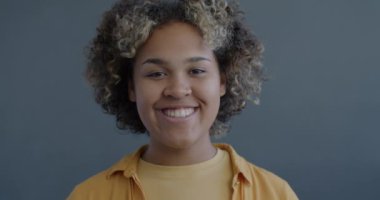 Gri arka planda memnuniyetini ifade eden el hareketlerini gösteren neşeli Afrikalı Amerikalı kadının yavaş çekim portresi.