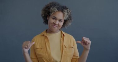 Gururlu Afrikalı Amerikalı kadının yavaş çekimde çekilmiş portresi. Kendini mutlu ve tatmin olmuş hissediyor. Gri arka plandaki kameraya bakıyor.