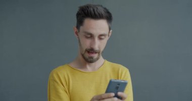 Akıllı telefonla mesajlaşan heyecanlı bir adamın portresi alete işaret ediyor ve gri arka planda iyi haberlerin keyfini çıkartıyor. İyi haber ve online iletişim konsepti.