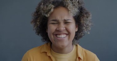 Gri arka planda kameraya bakıp gülen neşeli Afrikalı Amerikalı kadının yavaş çekim portresi. İnsanlar ve olumlu duygu kavramı.