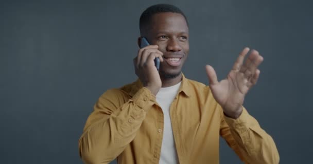 灰色の背景で会話を楽しんでいる携帯電話で話している楽しいアフリカ系アメリカ人の男性の肖像画 コミュニケーションと携帯電話のコンセプト — ストック動画