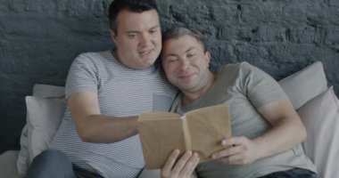 Evde edebiyatın ve romantik anın tadını çıkarırken yatakta kitap okuyan mutlu eşcinsel çift. Zeki hobi ve homoseksüel ilişki kavramı.