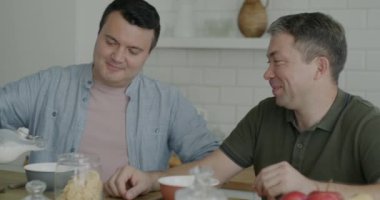 Aynı cinsiyetten neşeli erkekler kahvaltıda evde sütlü mısır gevreği yiyor. Sağlıklı beslenme ve LGBTQ ilişki kavramı.