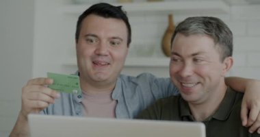 İnternetten alışveriş yapan aynı seks çifti kredi kartı ve dizüstü bilgisayarla apartmandaki internet mağazasından keyif alıyor. Bankacılık ve tüketim kavramı.